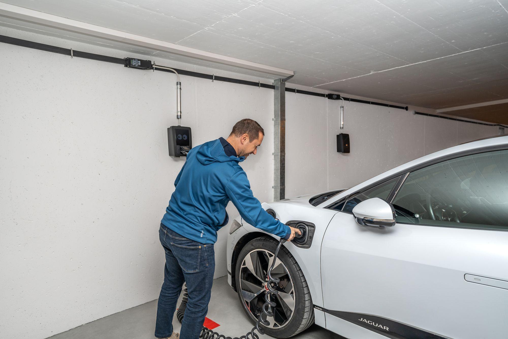 Condo owner plugging an electric car into a wall-mounted EV charger in an underground parking garage, the kind of installation Ontario condo boards review