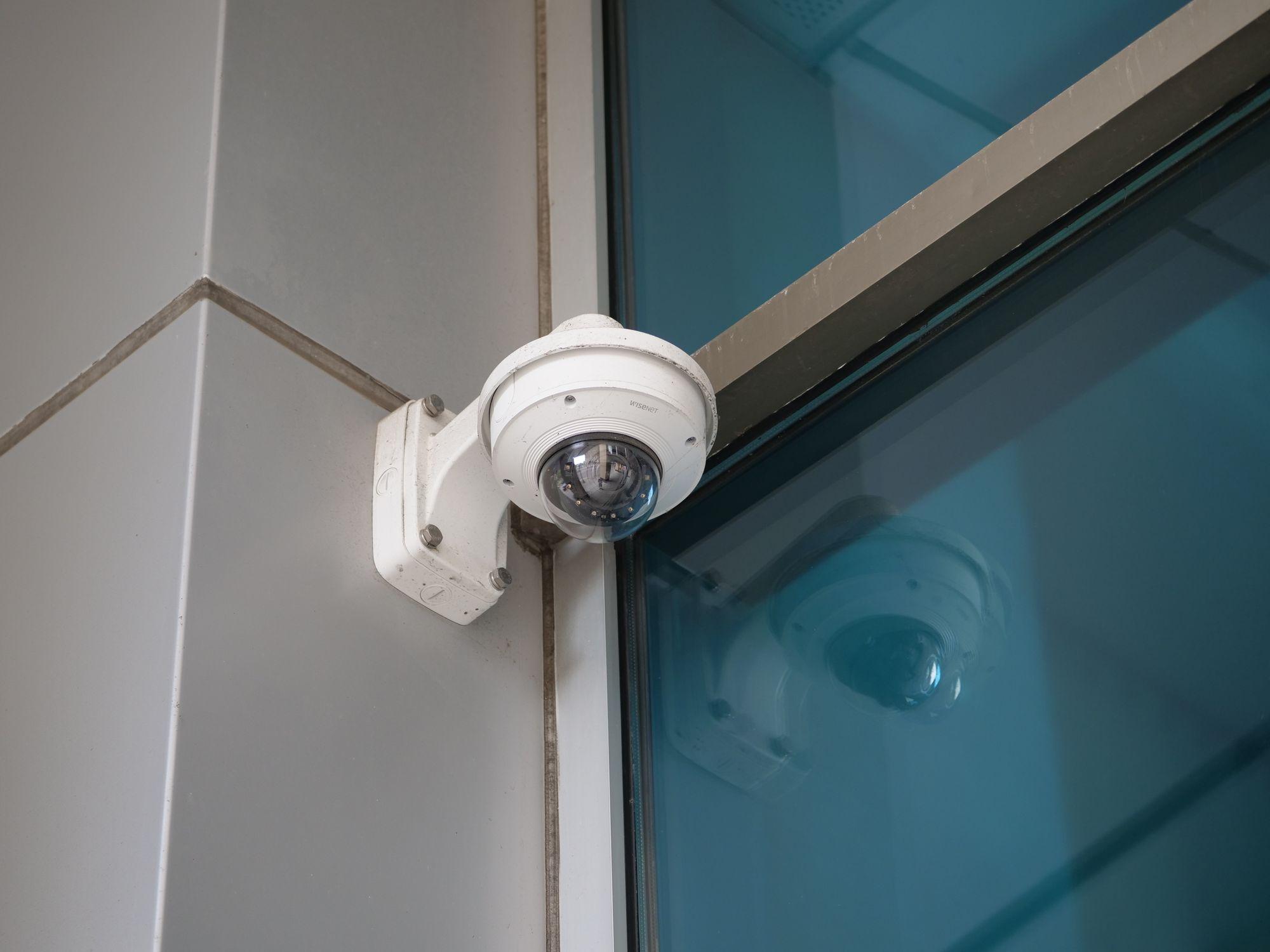 White dome security camera mounted on a wall beside the glass entrance of a residential condominium building