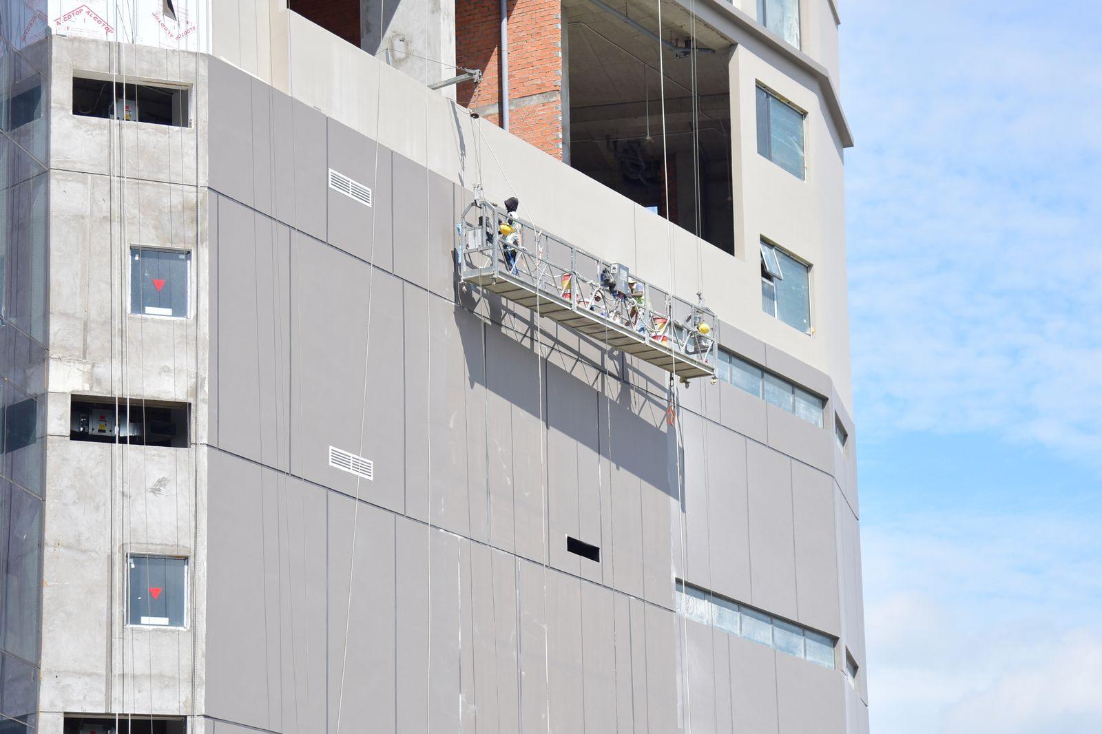 Contractors on a suspended platform repairing the facade of a high-rise residential tower