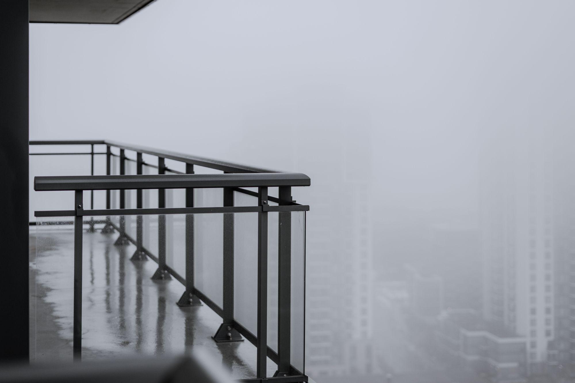 Wet concrete balcony slab with metal and glass guard railing on a Toronto high-rise condo, with fog over neighbouring towers